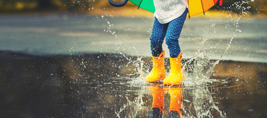 Feet of child in yellow rubber boots jumping in puddle in rain